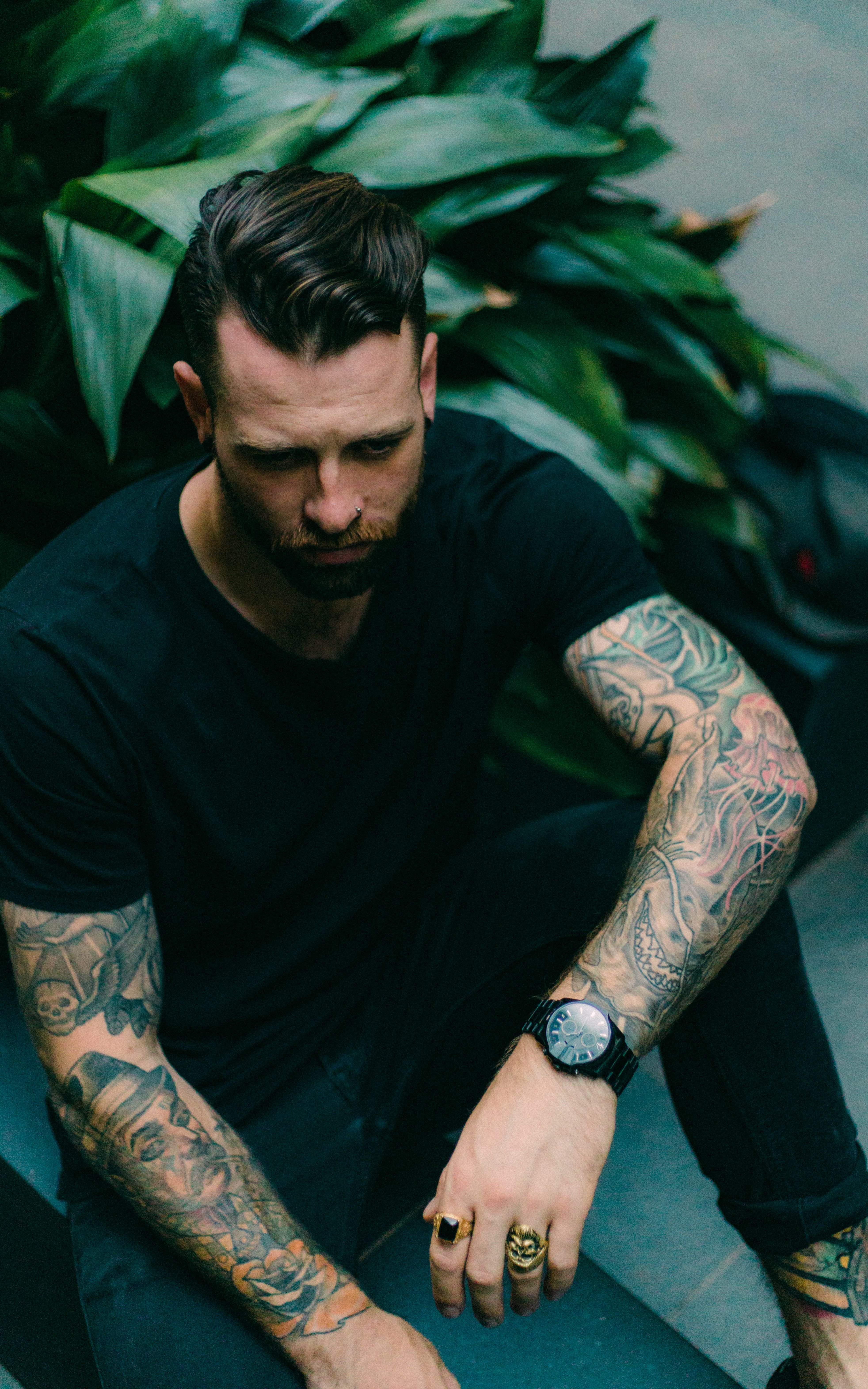Homem com sleeves tatuados sentado entre plantas